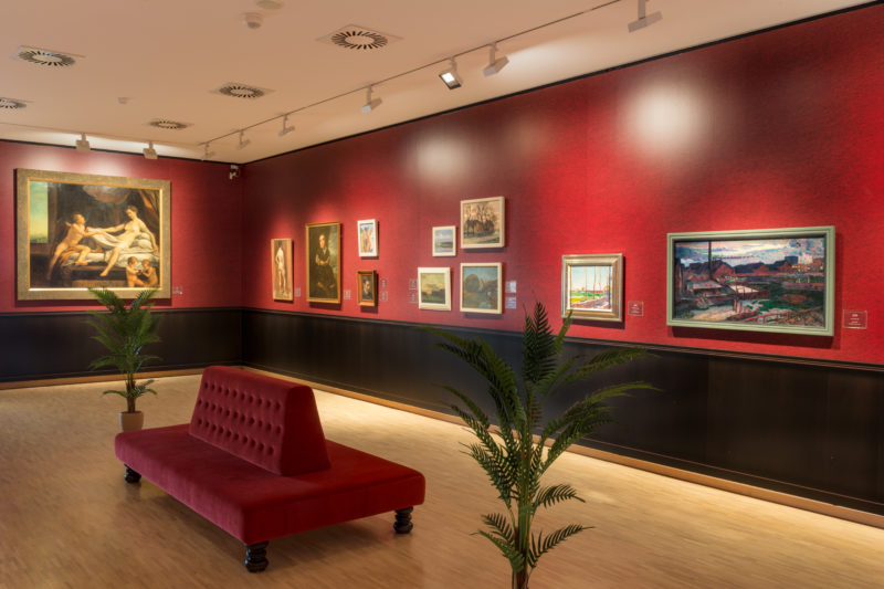 foto van tentoonstellingzaal, schilderijen hangen op een donkerrode wand.