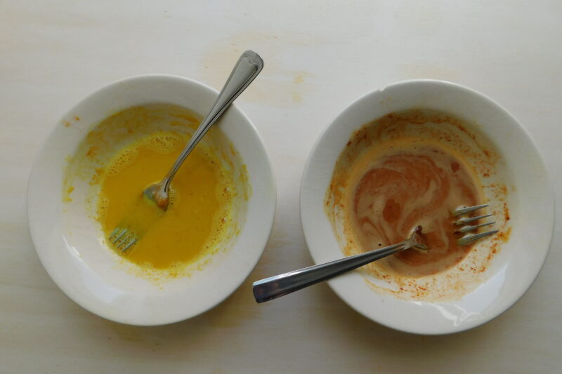 Twee schaaltjes; aan de geklutste dooier en het geklutste eiwit zijn kruiden toegevoegd, om de gewenste kleurmengsels te krijgen