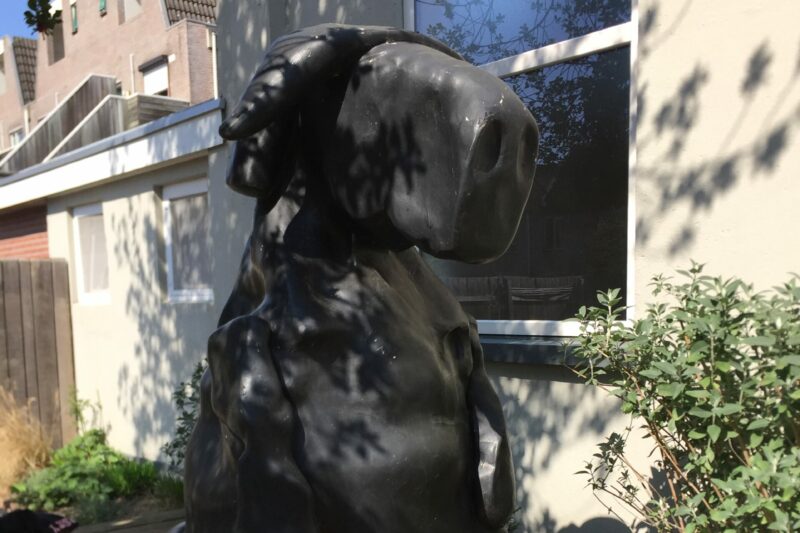 De sculptuur 'De zittende waterbuffel' van Tom Claassen, van een grote zwartw waterbuffel die op een bankje in de museumtuin zit